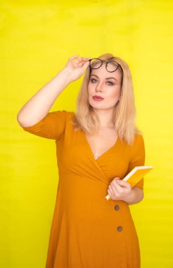 Sarı arka planda, elinde kitapla gözlüklü güzel sarışın kadın.