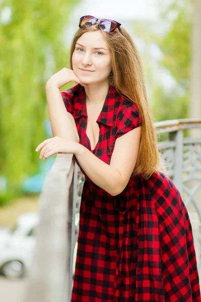 Portrait of a beautiful young woman with long brown hair in nature. Girl posing in a plaid dress on the balcony. — Stock Photo, Image