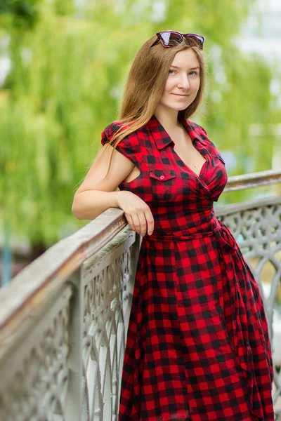 Retrato de uma bela jovem com longos cabelos castanhos na natureza. Menina posando em um vestido xadrez na varanda . — Fotografia de Stock