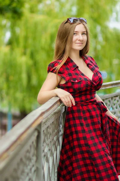 Retrato de una hermosa joven con el pelo largo y castaño en la naturaleza. Chica posando en un vestido a cuadros en el balcón . — Foto de Stock