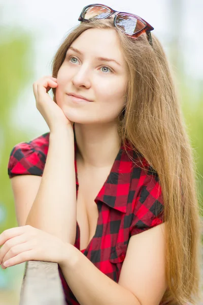 Retrato de uma bela jovem com longos cabelos castanhos na natureza. Menina posando em um vestido xadrez na varanda . — Fotografia de Stock