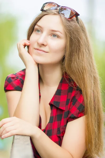 Portrait of a beautiful young woman with long brown hair in nature. Girl posing in a plaid dress on the balcony. — Stock Photo, Image