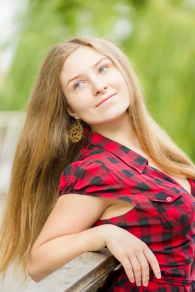 Retrato de una hermosa joven con el pelo largo y castaño en la naturaleza. Chica posando en un vestido a cuadros en el balcón . — Foto de Stock