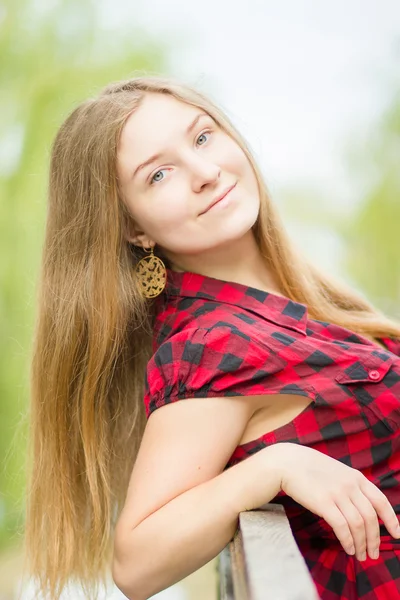 Retrato de una hermosa joven con el pelo largo y castaño en la naturaleza. Chica posando en un vestido a cuadros en el balcón . — Foto de Stock
