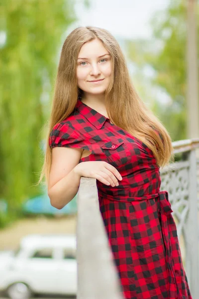 Retrato de una hermosa joven con el pelo largo y castaño en la naturaleza. Chica posando en un vestido a cuadros en el balcón . —  Fotos de Stock