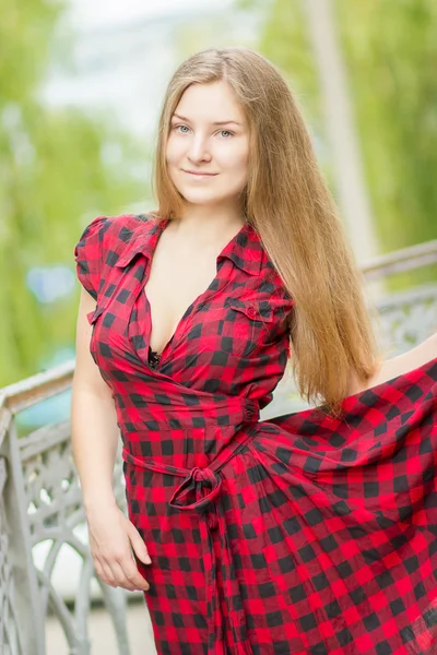 Portrait of a beautiful young woman with long brown hair in nature. Girl posing in a plaid dress on the balcony. — Stock Photo, Image