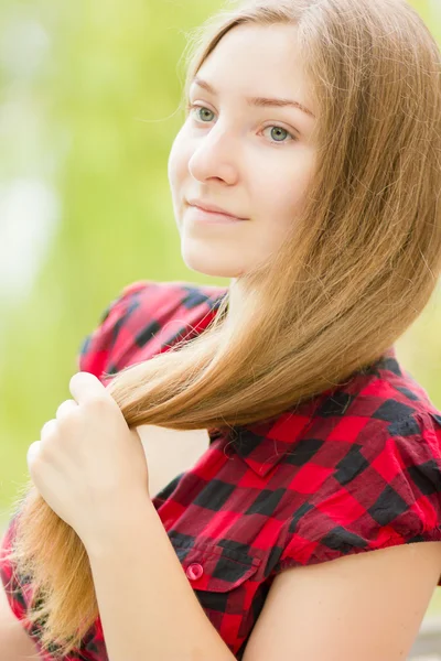 Portret van een mooie jonge vrouw met lang bruin haar in de natuur. meisje poseren in een geruite jurk op het balkon. — Stockfoto