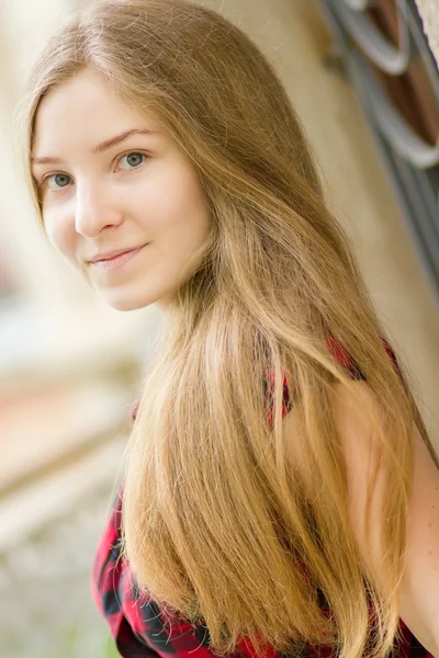 Porträt einer schönen jungen Frau mit langen braunen Haaren in der Natur. Mädchen posiert im karierten Kleid auf dem Balkon. — Stockfoto