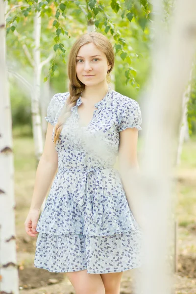 Portrett av en vakker ung kvinne med brunt langt hår på naturen i en kjole med blomstermønster. Jente som hviler i bjørkeskogen – stockfoto