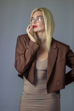 Sarışın, yuvarlak gözlüklü, eli dudaklarına yakın bir kadının stüdyo portresi. Gri arkaplan ve kopyalama alanı üzerine düşünceli düşünme kavramı.