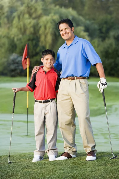 Hispanic father and son on hugging on golf course