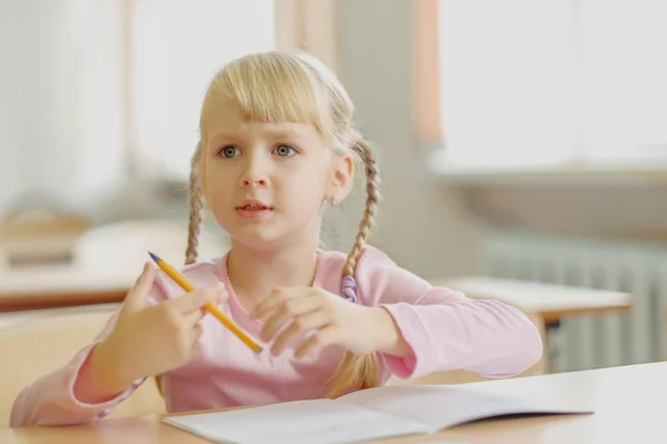 Niña rubia de cinco años sentada en el aula y escribiendo —  Fotos de Stock