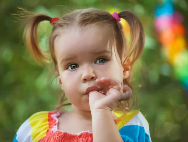 Cute little girl wearing colorful dress sucks her thumb — Stock Photo, Image