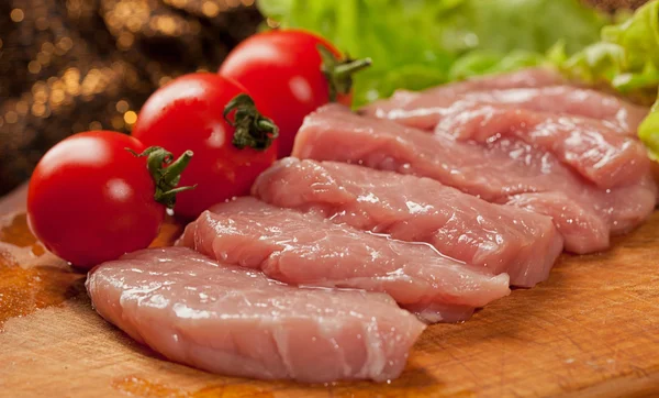 Raw pork on the wood board. Tomato and lettice — Stock Photo, Image