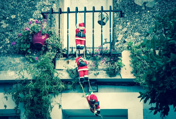 Three Santa Claus figures climbing up a wall into a window. Traditional Christmas decoration.  Toned photo. — Stock Photo, Image