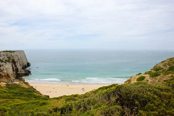 Praia na região algarvia de Portugal em dia nublado. Pessoas nadando e surfando. Uma vista de cima . — Fotografia de Stock