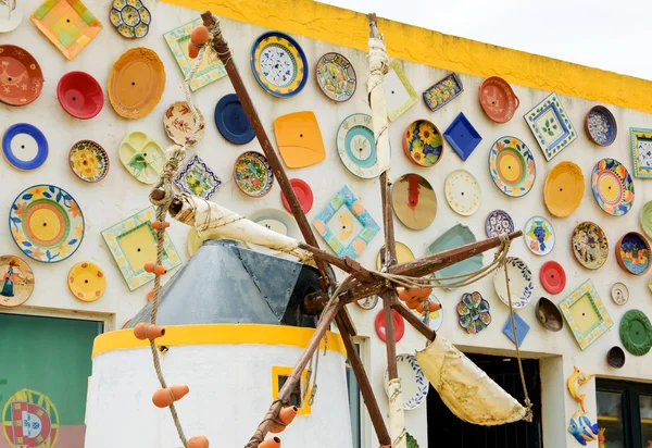 ALGARVE, PORTUGAL - 3 DE MAYO DE 2015: Placas tradicionales de cerámica colorida en la pared de la tienda de cerámica local y molino de viento decorativo. El Algarve es famoso por su cerámica y cerámica pintadas a mano. . — Foto de Stock