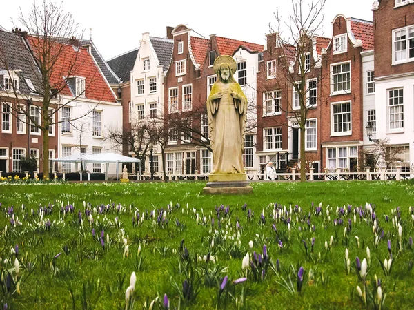 Estátua de Jesus cercada por flores de croco violeta e branca e casas históricas no pátio de Begijnhof. (Amesterdão, Países Baixos ) Fotos De Bancos De Imagens