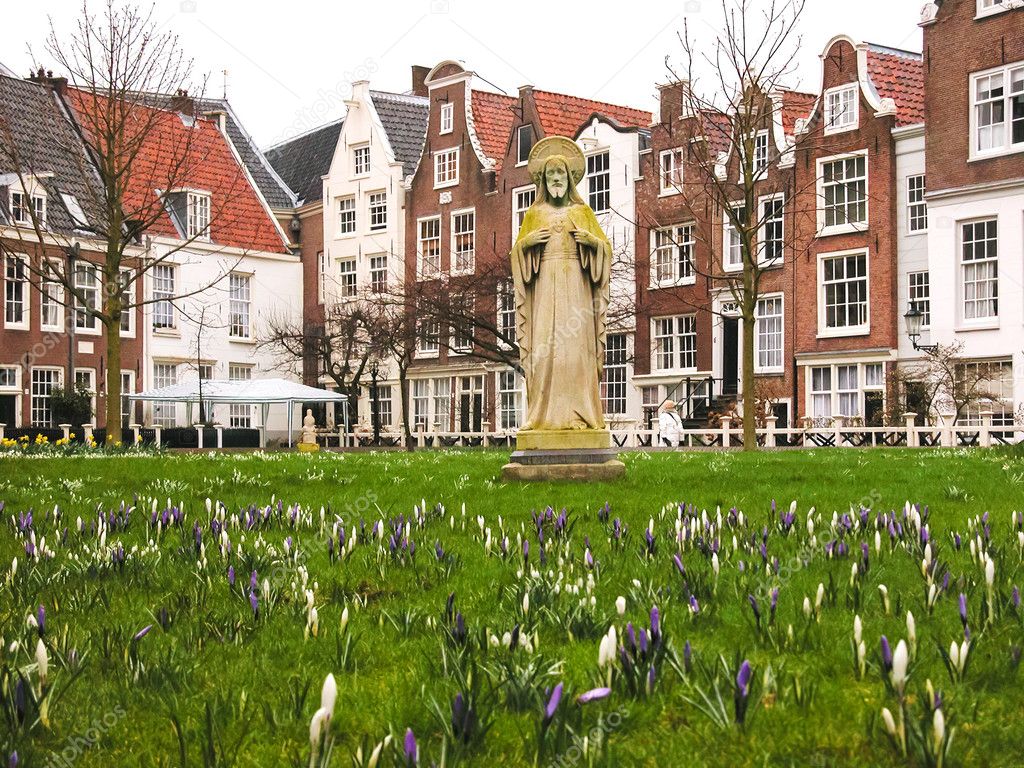 Jesus statue surrounded by violet and white crocus flowers and historic houses in Begijnhof courtyard. (Amsterdam, Netherlands)