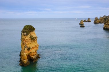 Güzel kaya oluşumları, taş kemerler ve Dona Ana Plajı'nda mağaralar ve ufukta yelkenli tekneler (Lagos, Algarve kıyıları, Portekiz) akşam ışığında.