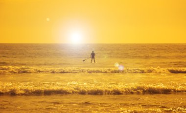 Gün batımında kürek çekerken kürek çeken adamın silueti. Lens parlama etkisi ile tonda fotoğraf.