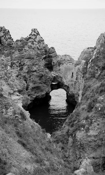 Água do oceano vista através de um buraco nas rochas. Arcos de pedra, grutas, formações rochosas na Praia da Dona Ana (Lagos, costa algarvia, Portugal) à luz da noite. Foto envelhecida. Preto e branco . — Fotografia de Stock