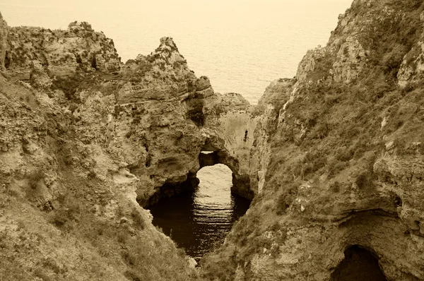 Eau de mer vue à travers un trou dans les roches. Arcs en pierre, grottes, formations rocheuses à Dona Ana Beach (Lagos, côte de l'Algarve, Portugal) dans la lumière du soir. Photo vieillie. Sepia . — Photo