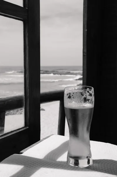 Cold beer on cafe terrace with the view on the ocean beach through the opened window. Algarve, Portugal. A game of light an shadow. Aged photo. Black and white.