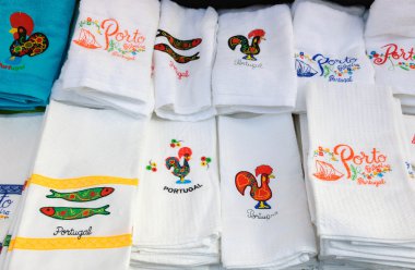 Souvenir towels with embroidery of the Galo de Barcelos (Barcelos Rooster) and other traditional symbols of Portugal at the street market in Porto (Portugal). clipart