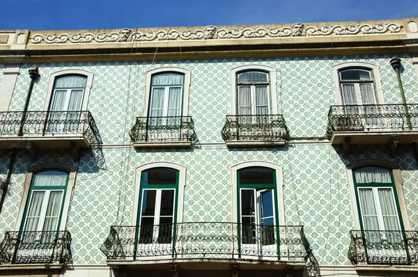 Edificio típico antiguo en el centro de Lisboa (Portugal). Coloridas baldosas cerámicas (azulejos) con patrón floral, balcones y borde del techo con caras masculinas . — Foto de Stock