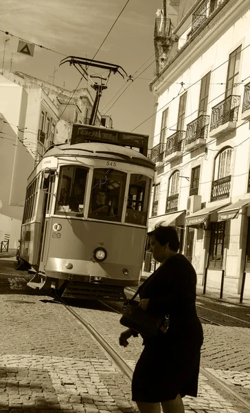 LISBOA, PORTUGAL - 22 de abril de 2015: Mulher não identificada a passar diante de um velho eléctrico que circula no centro histórico de Lisboa. Este pequeno eléctrico é um dos símbolos mais reconhecidos de Lisboa . — Fotografia de Stock