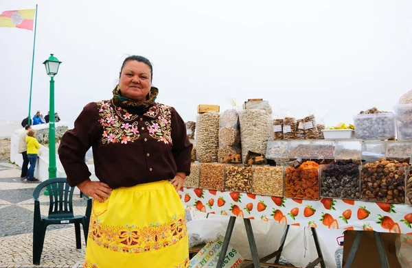 NAZARE, PORTUGAL - MAY 1, 2015: An unidentified lady in traditional  Portuguese costume sells nuts, dried fruits and local candies at the street market. — Stock Photo, Image