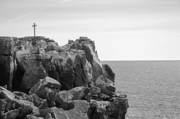 Kříž na skalnatém vrcholku nad oceánem. Peniche, Portugalsko. Starší fotografie. Černá a bílá. — Stock fotografie