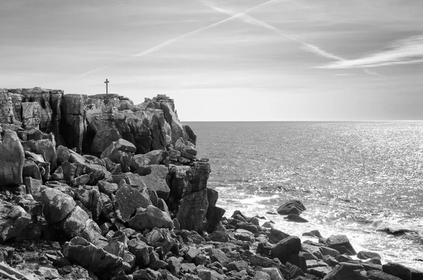 Atravesse o cume rochoso sobre o oceano. Cruze no céu - traço de avião. Peniche, Portugal. Foto envelhecida. Preto e branco . — Fotografia de Stock