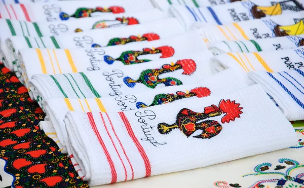 Souvenirhandtücher mit Stickereien des galo de barcelos (barcelos Hahn) - traditionelles Symbol Portugals - auf dem Straßenmarkt in porto (portugal). Selektiver Fokus auf die nächstgelegenen Handtücher. Stockbild