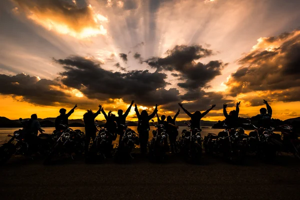 Silhouet van groep vrienden permanent met motorfiets in sunse Stockfoto
