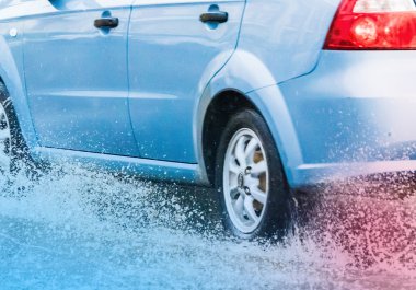 Araba yağmuru su sıçratıyor.