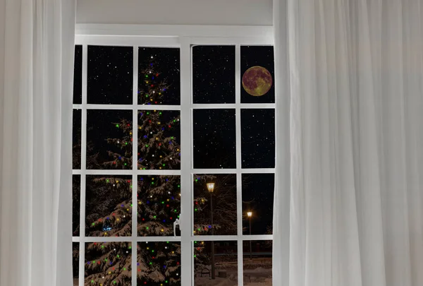 在节日圣诞树前从窗户往外看 是用五彩缤纷的花环装饰的 免版税图库图片