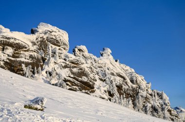 Kışın buz tutmuş taş kayalar mavi gökyüzü arka planında karla kaplı.