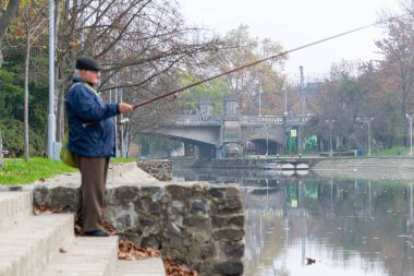 Timisoara, Romanya - 22 Kasım 2012: Ön planda balık tutan bir adamla Bega Nehri manzarası. Gerçek insanlar..