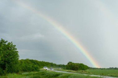A rainbow in the stormy dark sky over a road