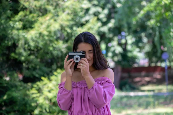 穿着粉色连衣裙的女人在公园里用老式胶卷相机拍照 — 图库照片