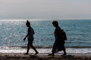 Sahilde yürüyen insanların silueti. Tanınmayan insanlar. Denize odaklan.