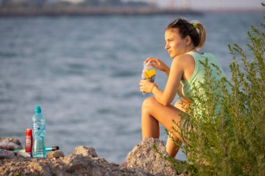 2 Mai, Romanya - 05 Ağustos 2021: Bir kayanın üzerinde oturan, balık tutan ve ayçiçeği tohumu yiyen kadın. Gerçek İnsanlar