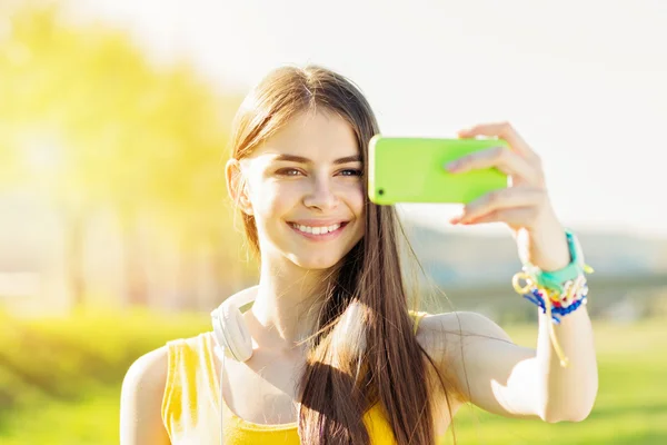 Teini tyttö hymyilee ottaen selfie älypuhelimella — kuvapankkivalokuva