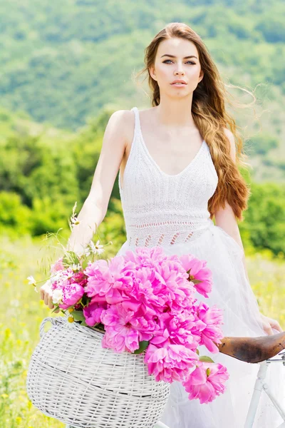 Belle jeune femme avec vélo et panier avec bouquet de pivoines — Photo