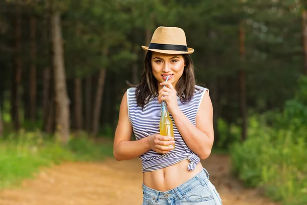 Jonge vrouw in casual kleding en stro fedora hoed limonade drinken uit de fles — Stockfoto