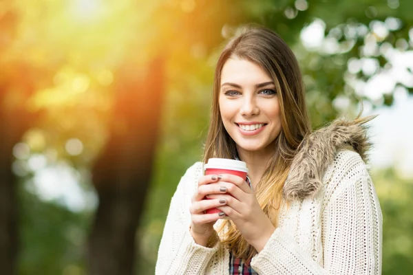 Jonge vrouw met afhaalmaaltijden koffie in park in het najaar — Stockfoto