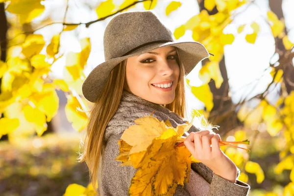 Beautiful young woman in park in autumn holding leaves — Stock Photo, Image