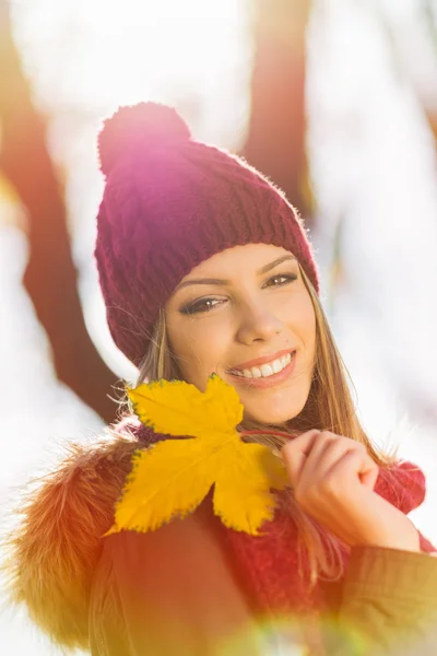 Beauitufl young woman in park in autumn holding a yellow leaf — Stock Photo, Image